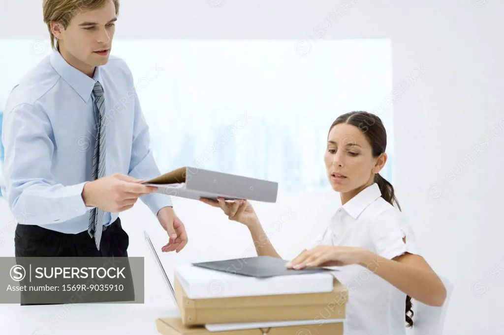 Professional woman handing binder to colleague from stack of many binders