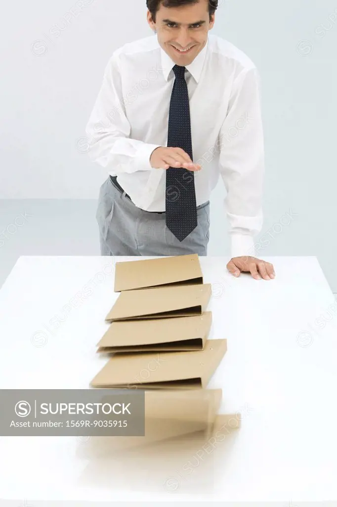 Businessman knocking over binders, smiling at camera