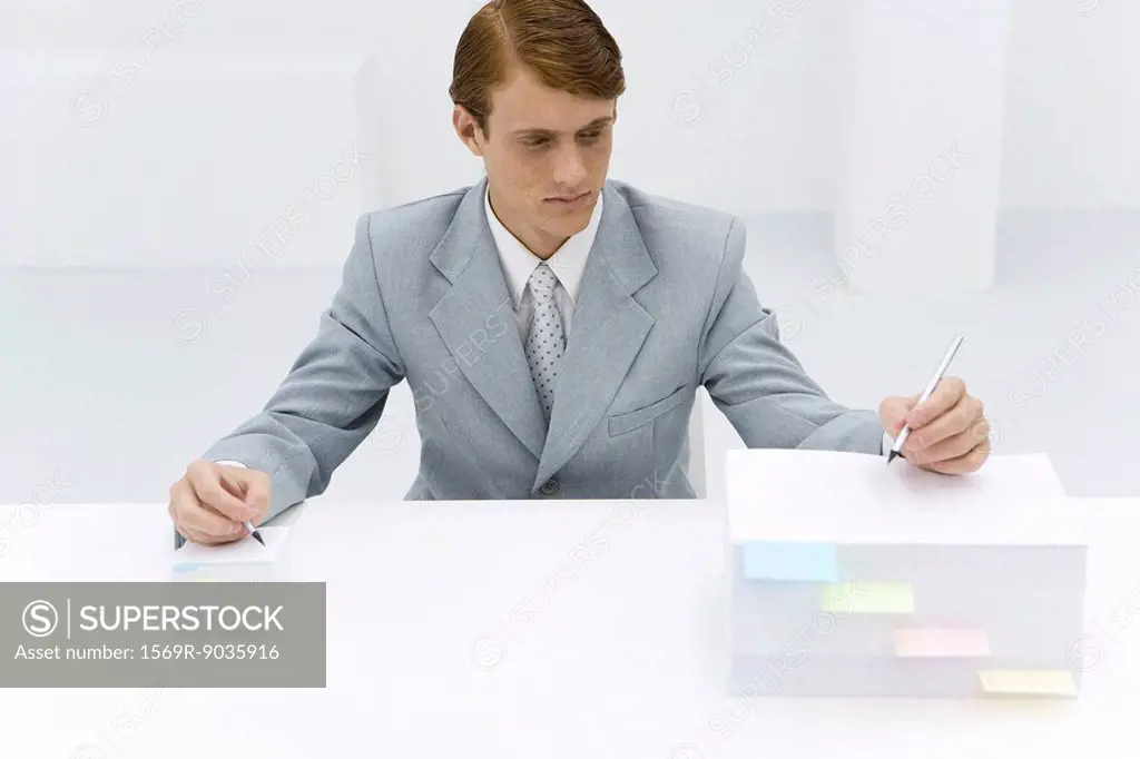 Businessman writing on two stacks of paper, one large, one small, pencil in each hand