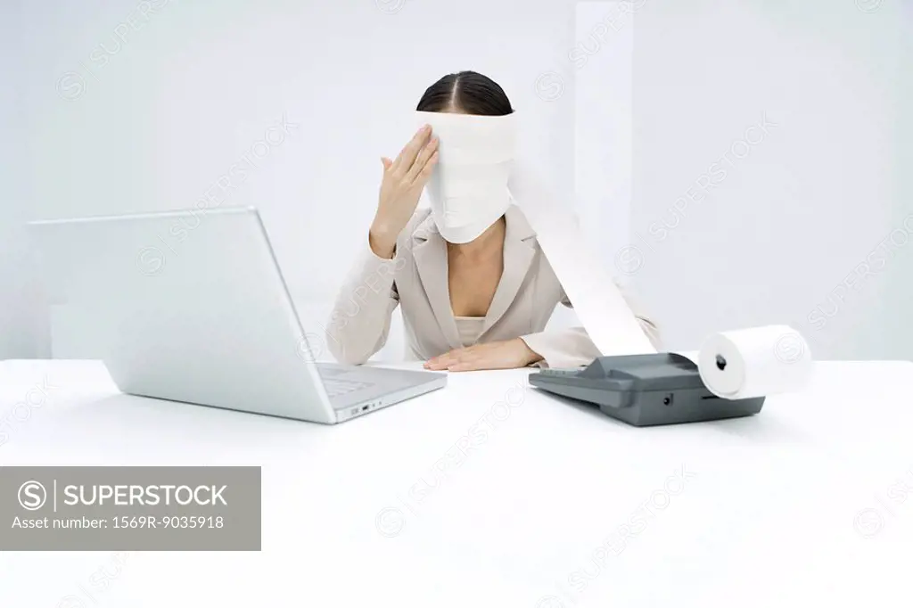 Woman sitting behind adding machine, roll paper wrapped around her head