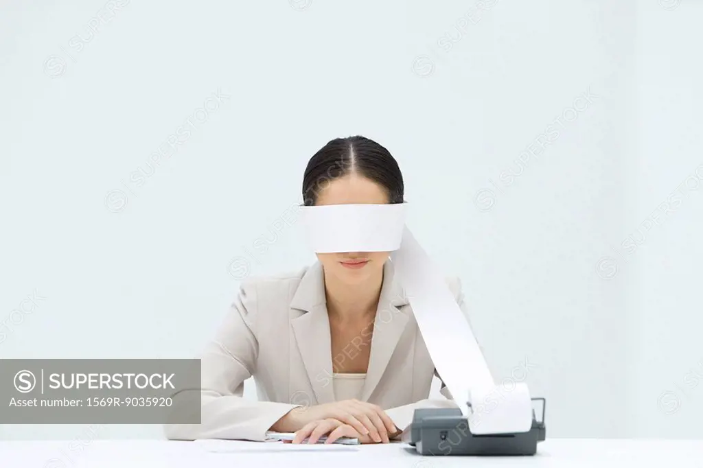 Woman sitting at desk, tape from an adding machine wrapped around her eyes, arms folded