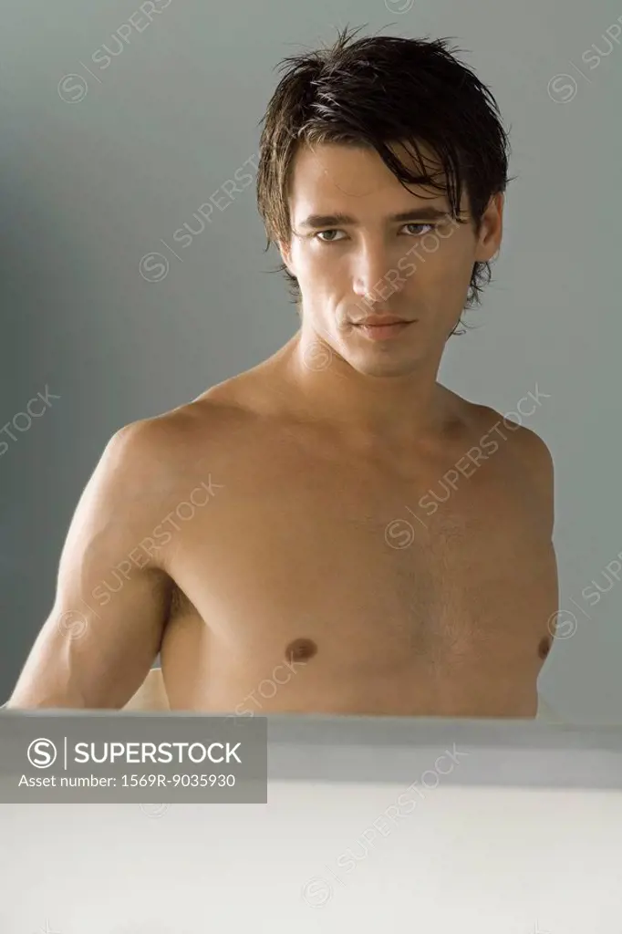 Bare-chested man looking at self in mirror, cropped view of reflection