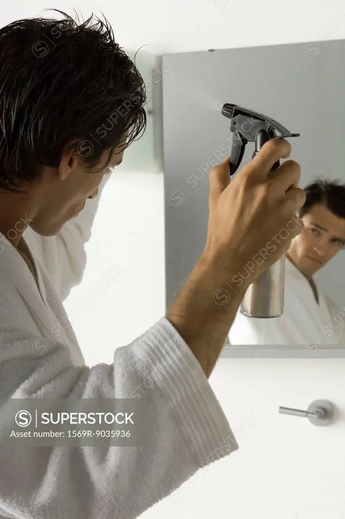 Man looking at himself in mirror, spritzing hair with spray bottle