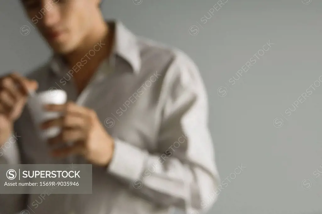 Man holding disposable coffee cup, defocused, cropped