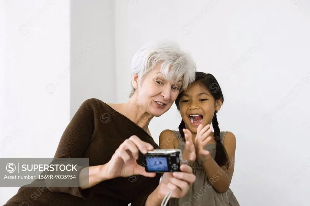 Senior woman photographing self and granddaughter with digital camera, both laughing