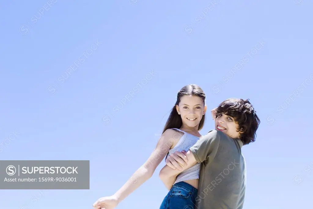 Teenage boy picking up little sister, hugging, low angle view
