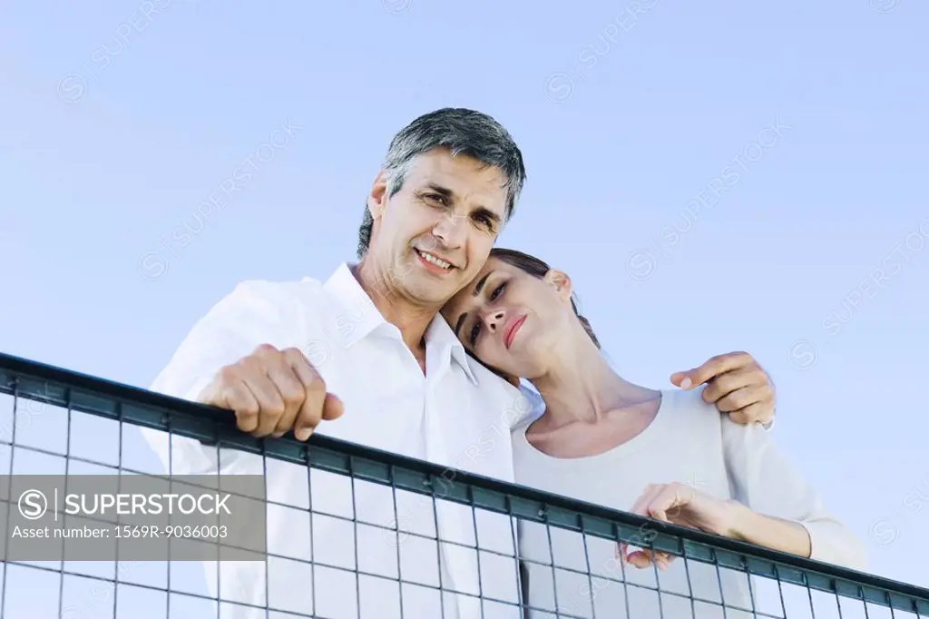 Couple looking down over wire fence at camera, low angle view