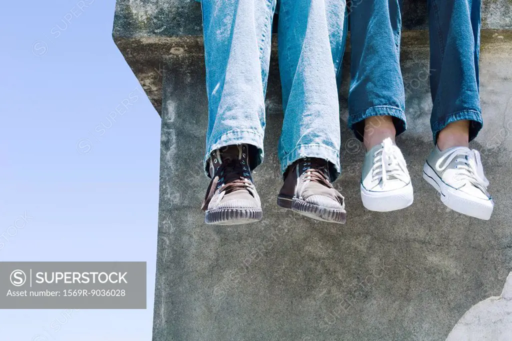 Two pairs of legs dangling over concrete ledge