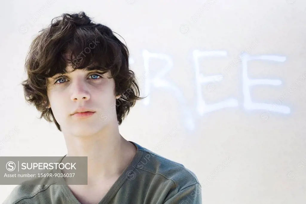 Teenage boy looking at camera, in front of graffiti