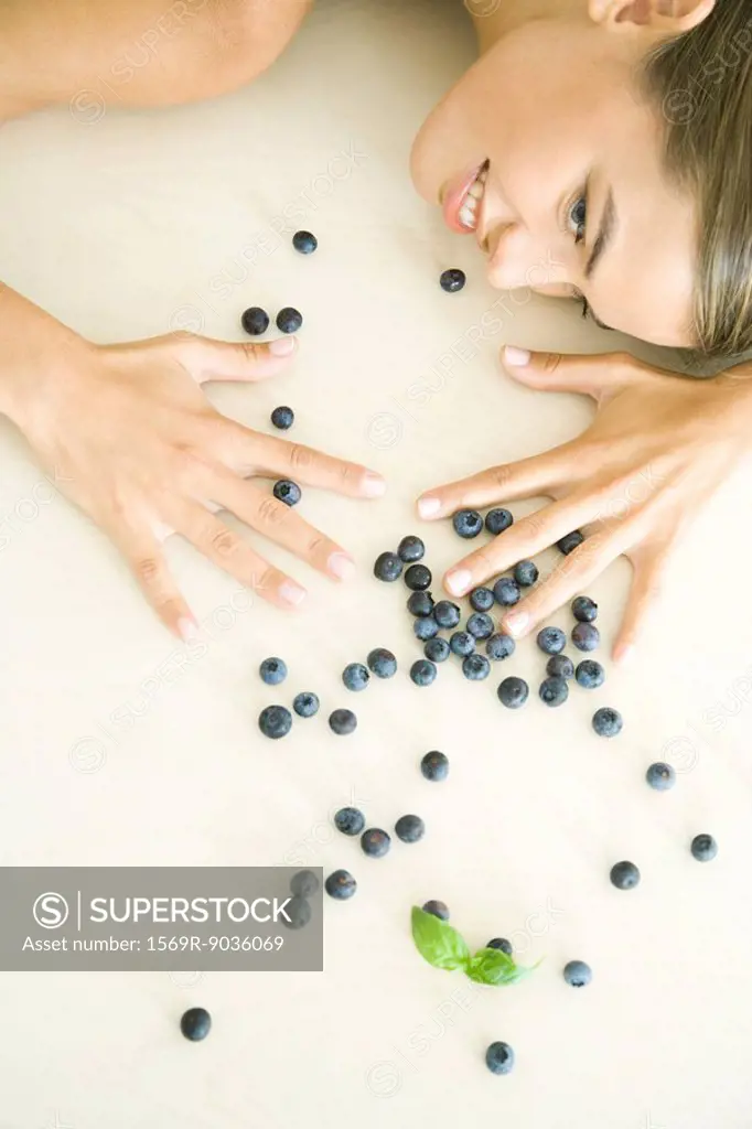 Fresh blueberries scattered across counter, young woman spreading hands over them