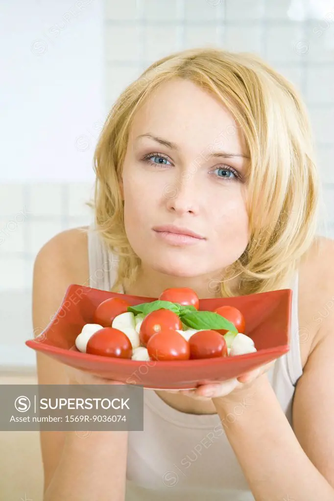 Woman holding up a plate of Caprese salad, looking at camera