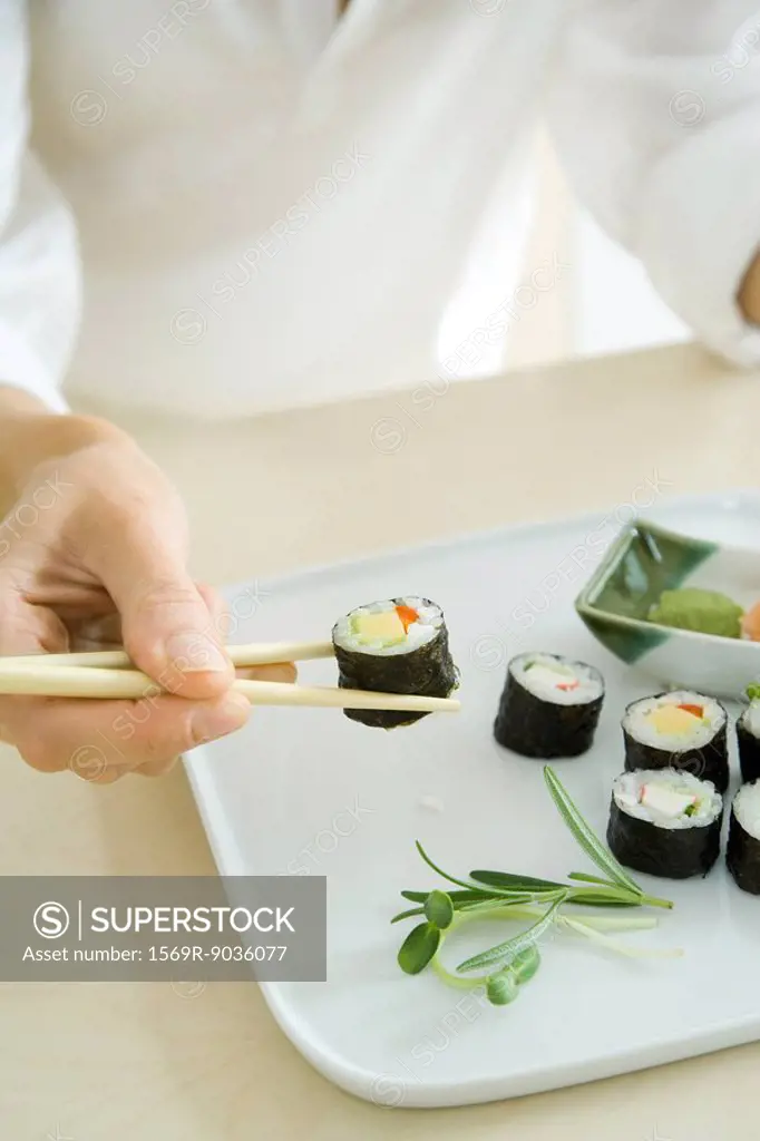 Person using chopsticks to pick up a sushi roll, cropped view