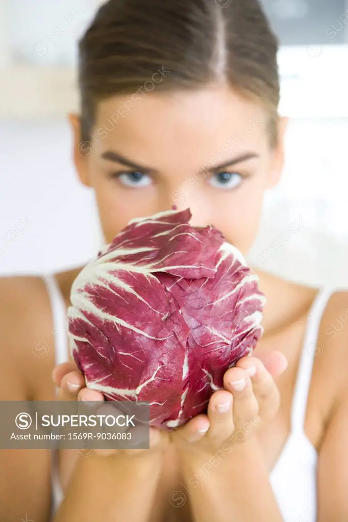 Woman holding a head of radicchio lettuce, partially obscuring her face, looking at camera