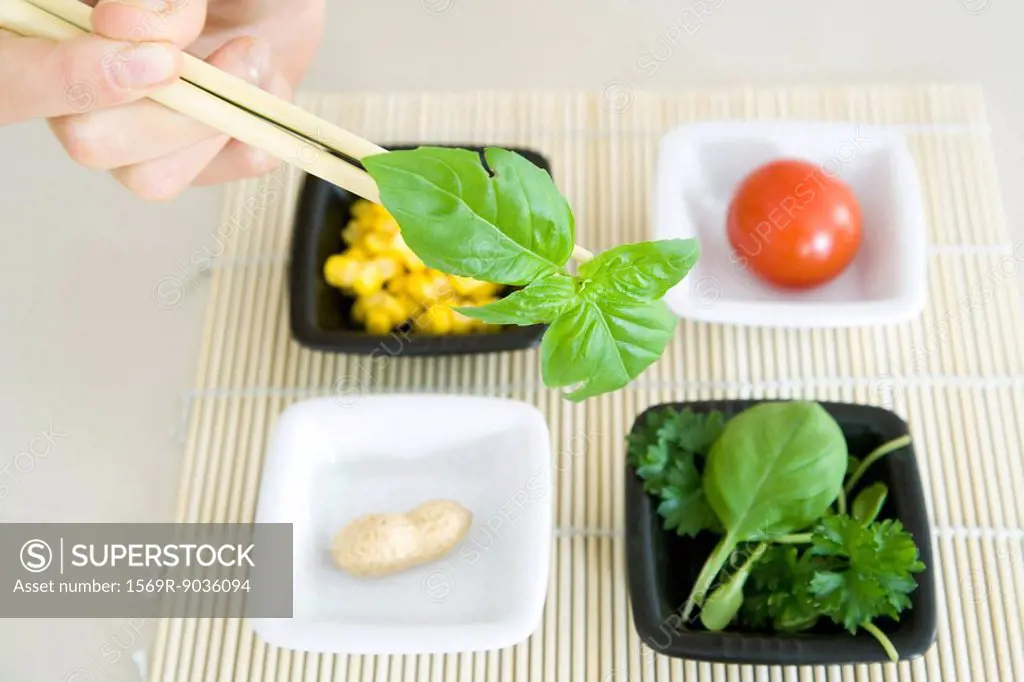 Chopsticks holding up a sprig of herb several small plates of food