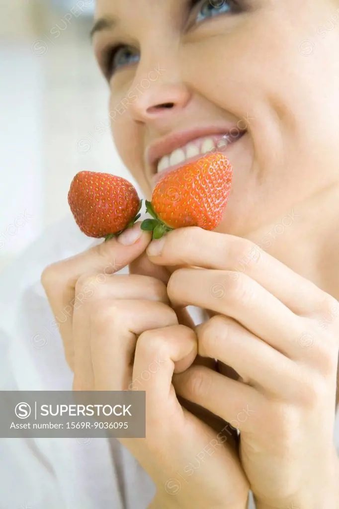 Woman holding a pair of strawberries, smiling, looking up, cropped