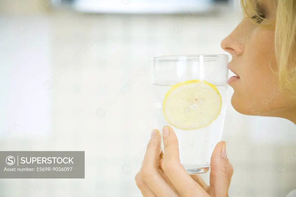 Woman holding a glass of water with a slice of lemon up to her lips, profile