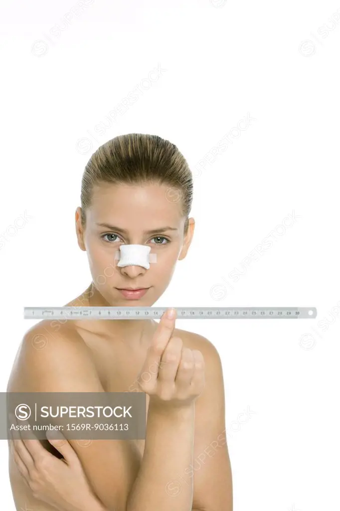 Woman with bandaged nose, holding ruler, looking at camera