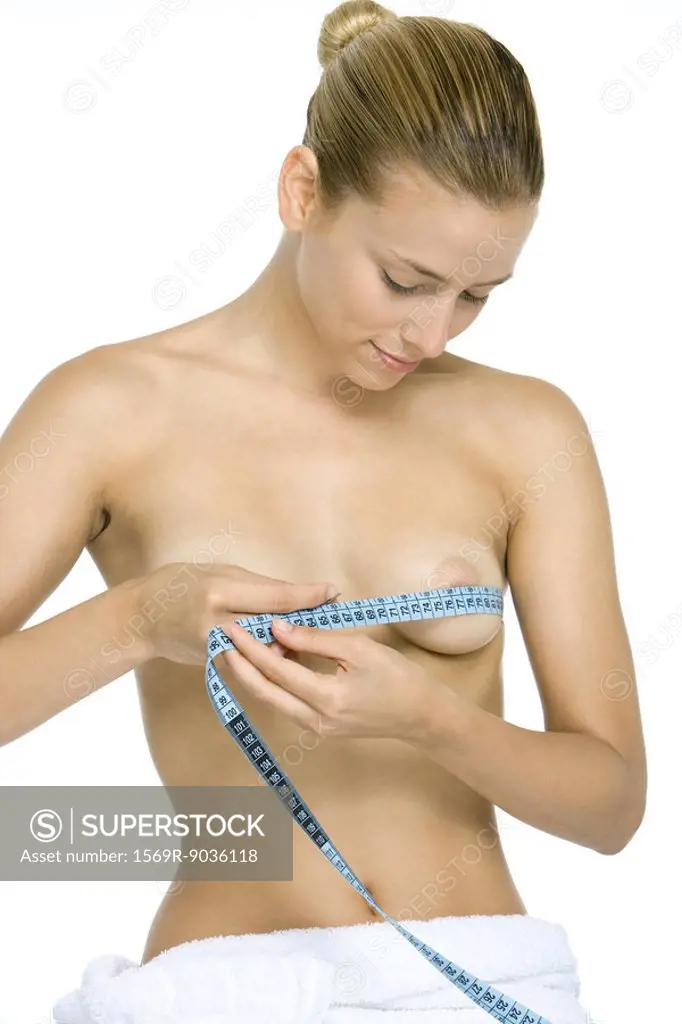 Woman wrapping measuring tape around chest, looking down at breasts, smiling