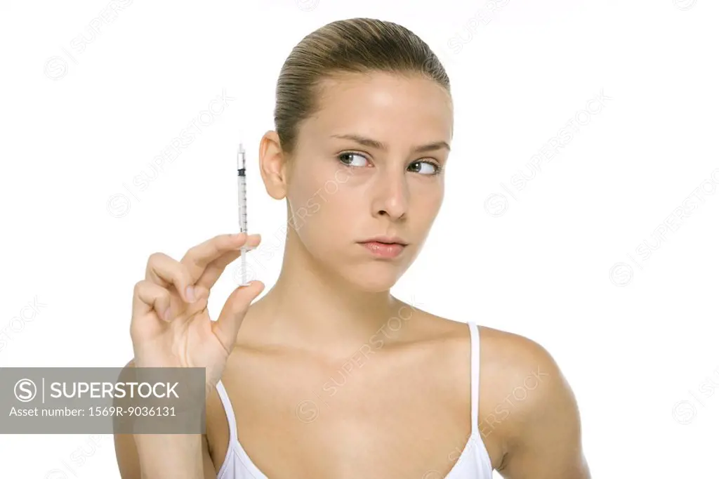 Young woman looking at syringe, close-up