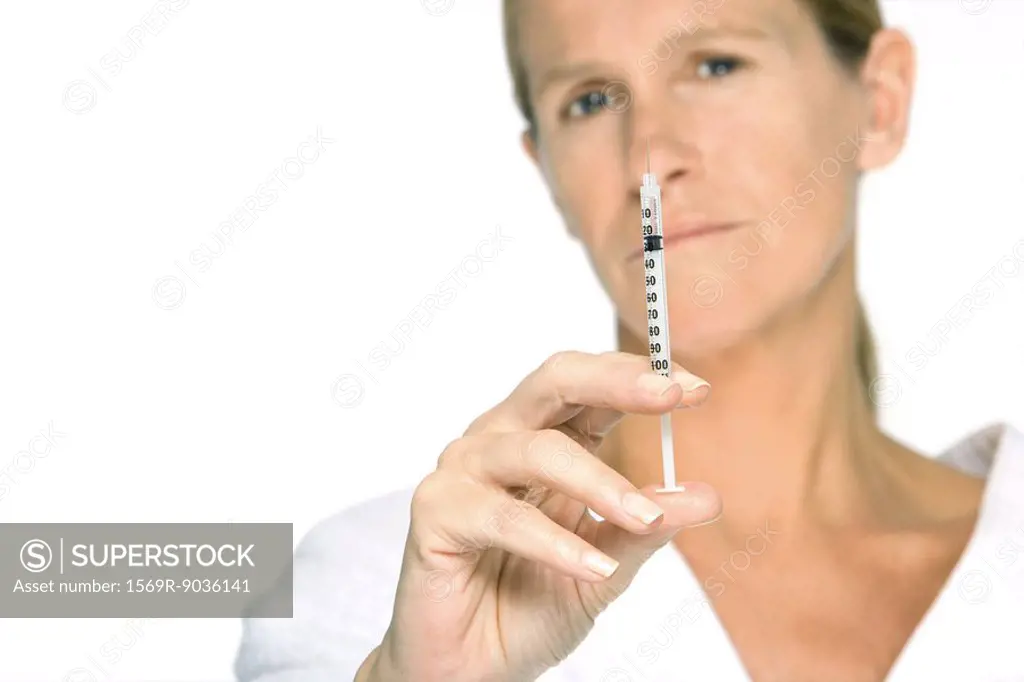 Woman holding up syringe, looking at camera