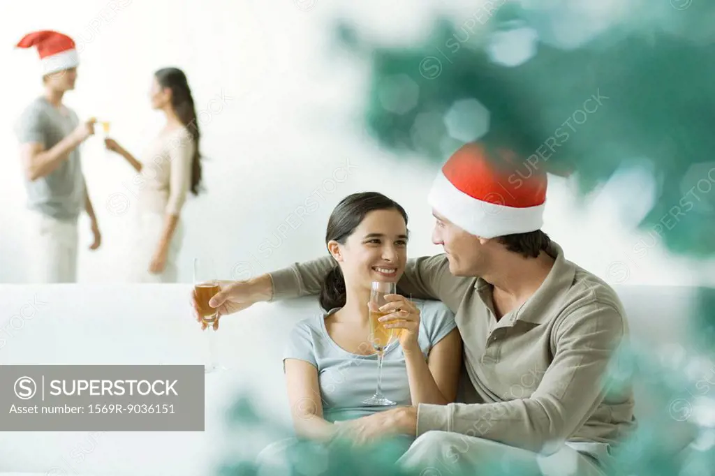 Couple sitting on sofa, drinking champagne, man wearing Santa hat