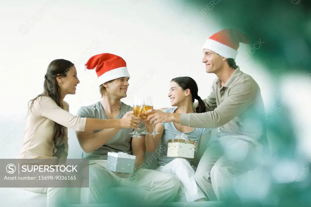 Two couples toasting and exchanging gifts, men wearing Santa hats