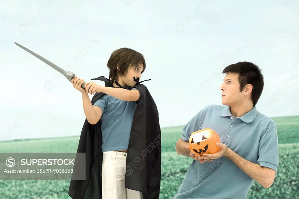 Father and son playing, man holding jack o´ lantern, boy swinging sword