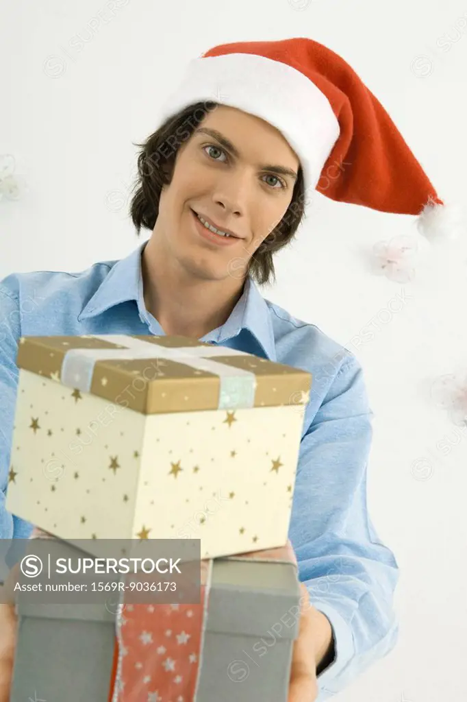Young man holding Christmas gifts toward camera, smiling
