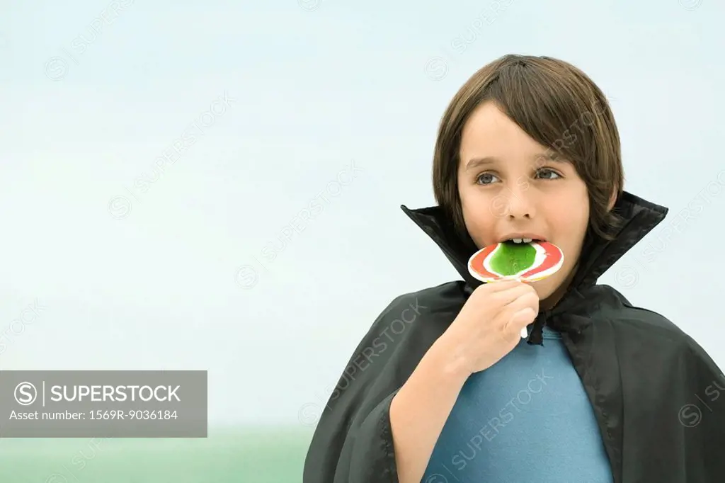 Boy wearing vampire cape, eating large lollipop, portrait
