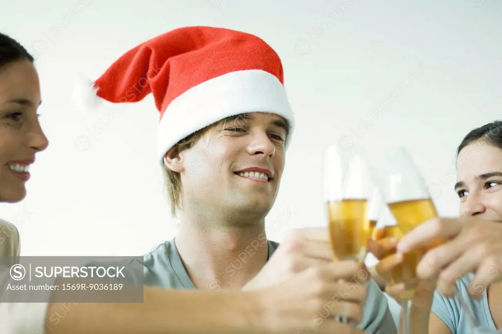Adult friends clinking champagne glasses, smiling, focus on man in Santa hat, cropped