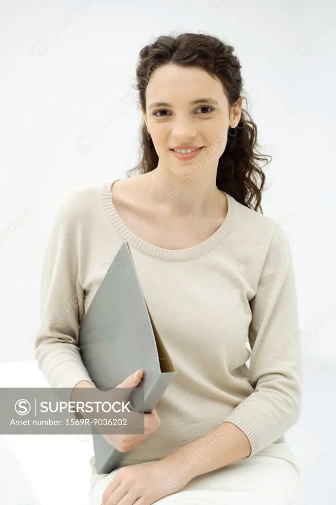 Young woman holding binder, smiling at camera