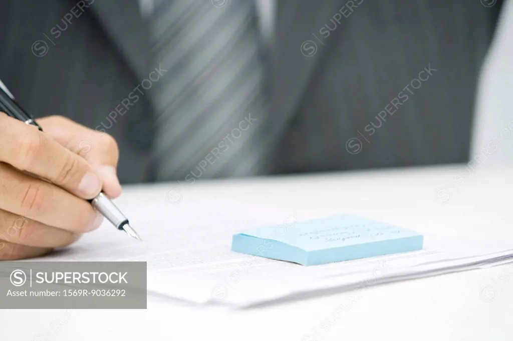 Man with adhesive note and document, holding pen, cropped view