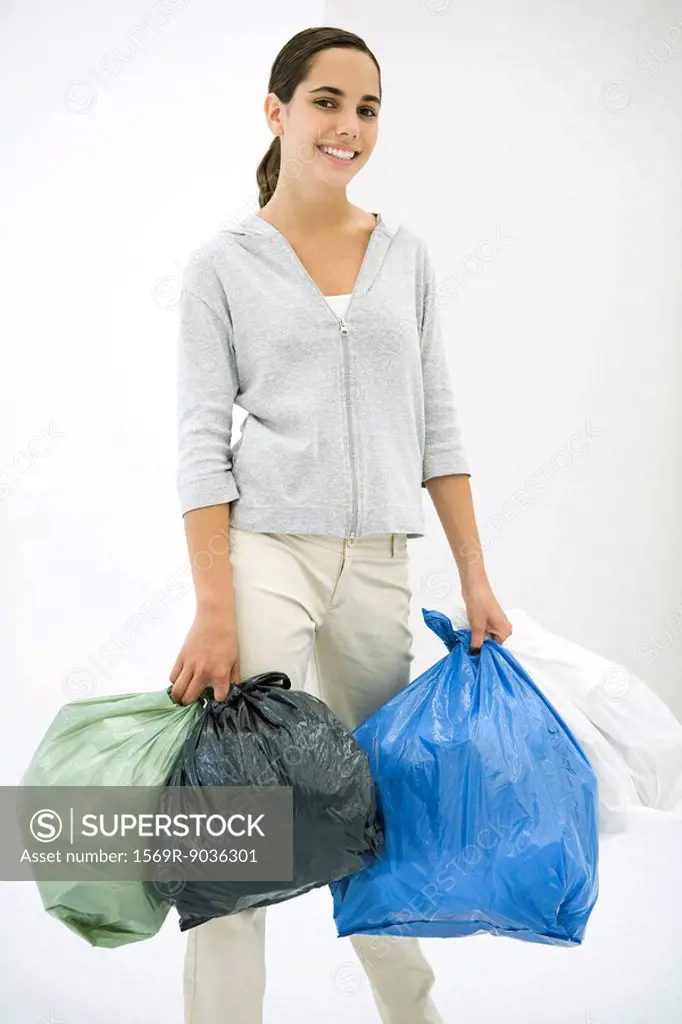 Teen girl carrying several garbage bags, smiling at camera