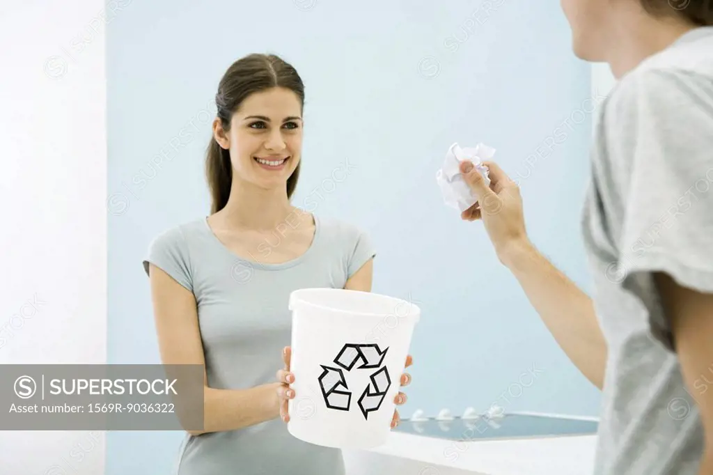 Man aiming paper ball toward recycling bin in woman´s arms, cropped view