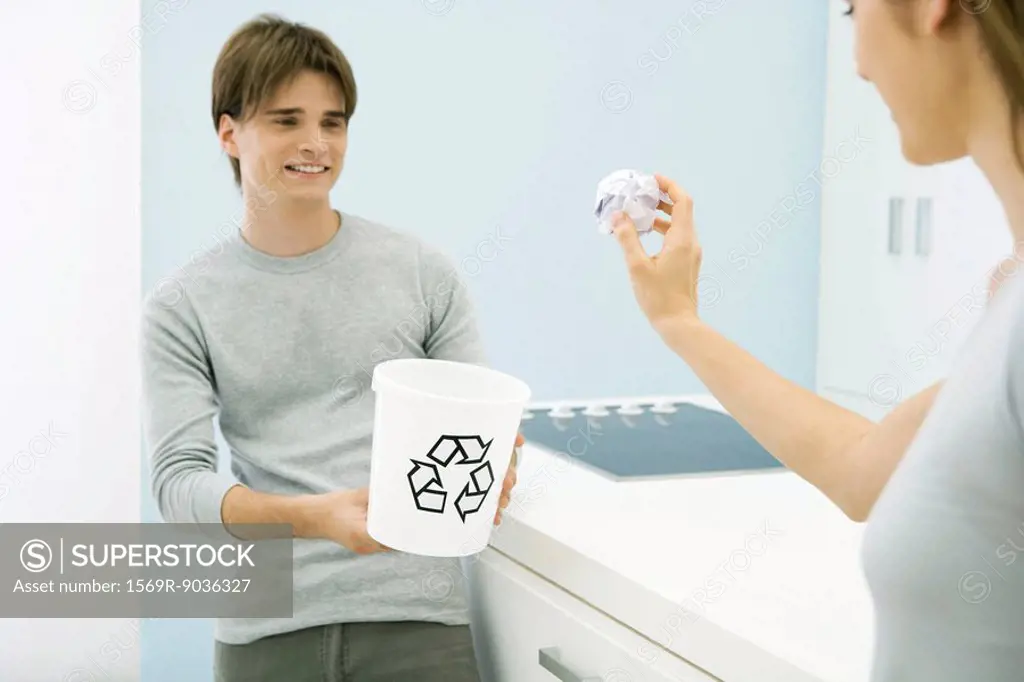 Woman aiming paper ball at recycling bin in young man´s hands, cropped view