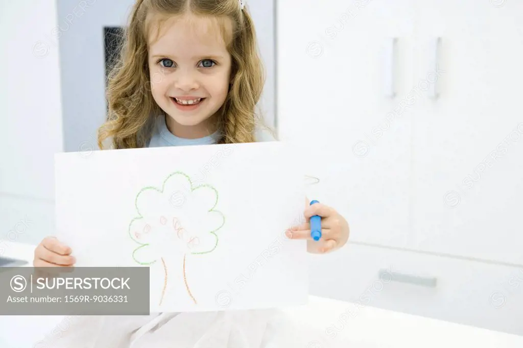 Little girl holding drawing of tree, smiling at camera