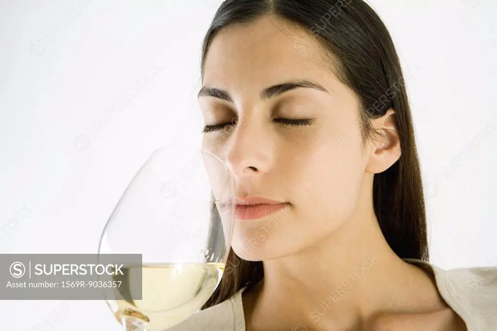 Woman smelling glass of white wine, eyes closed