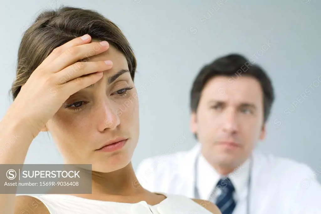 Woman holding head, looking down, doctor in background