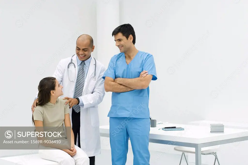 Doctor standing with hands on teen girl´s shoulders, male nurse standing nearby