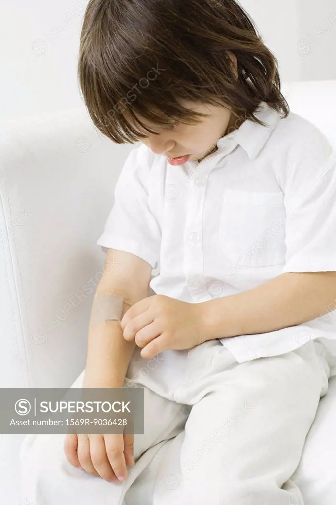Little boy picking at adhesive bandage on his arm, head down