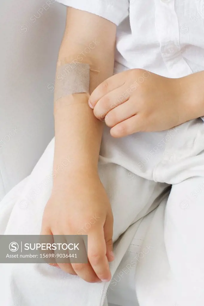 Little boy picking at adhesive bandage on his arm, cropped view