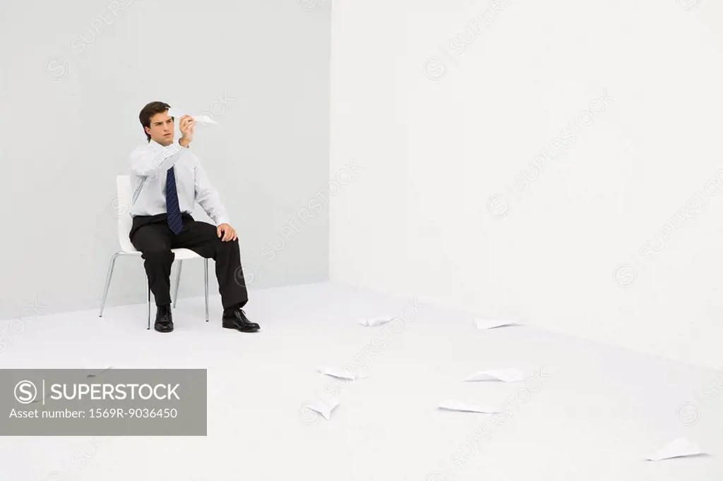 Young professional man sitting in corner, throwing paper airplanes
