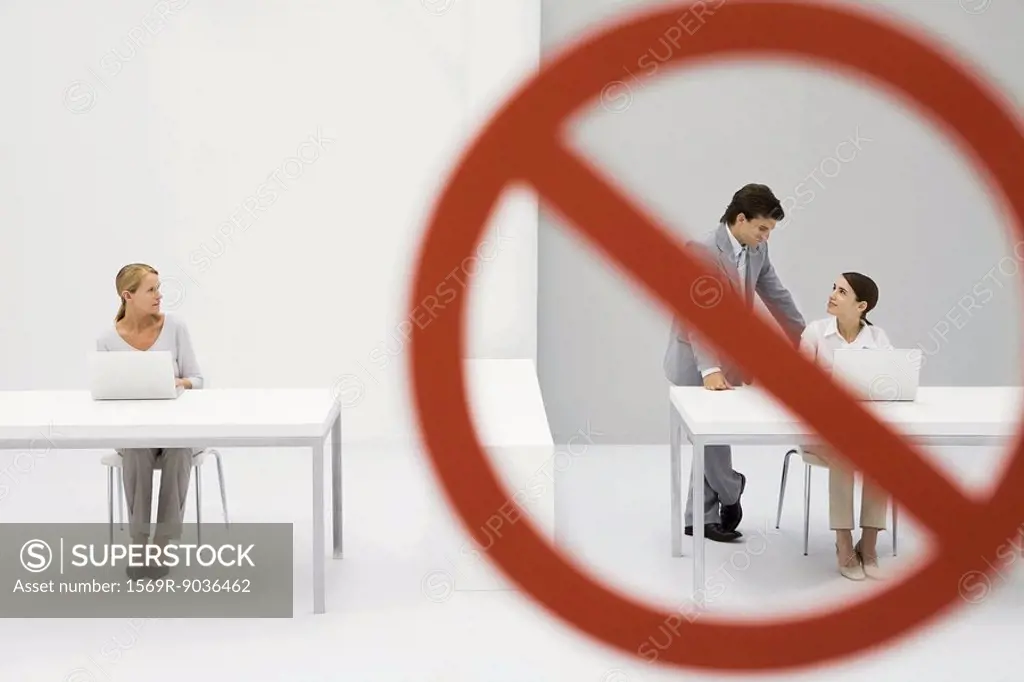 Warning sign across chatting male and female office workers, female colleague watching