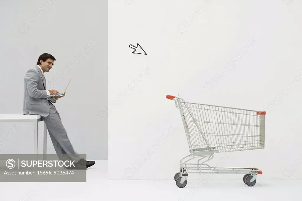 Businessman leaning against desk, shopping online, cursor pointing at shopping cart