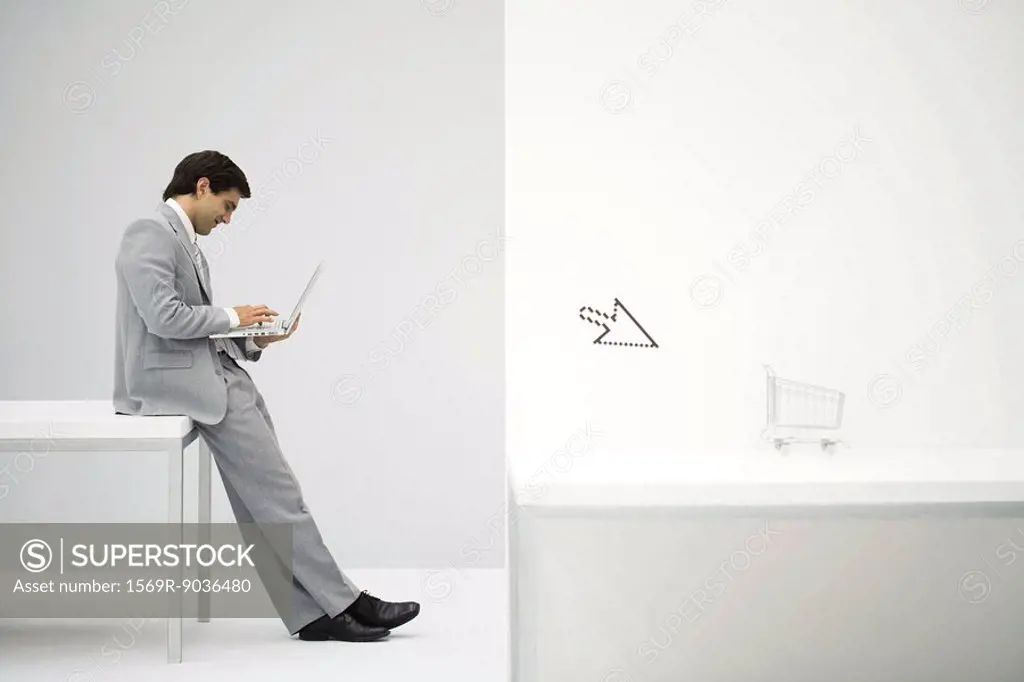 Businessman sitting on desk, shopping online, shopping cart and cursor in foreground