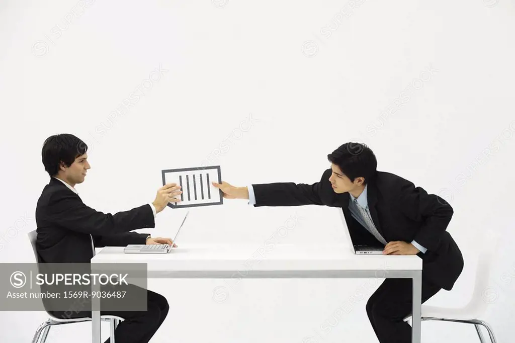 Two business associates sitting face to face at desk, one hand document to the other