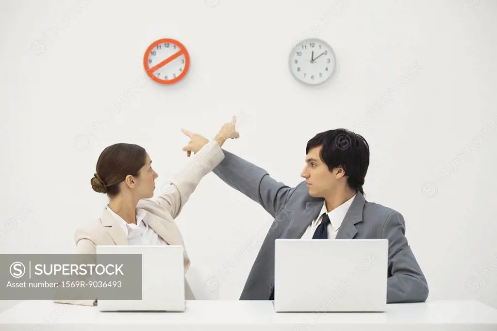 Professionals sitting at desk, pointing at clocks on wall behind them