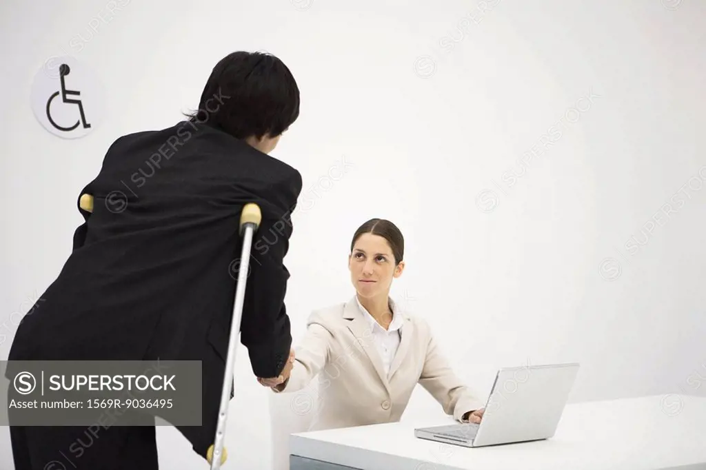 Professional woman shaking hands with man on crutches