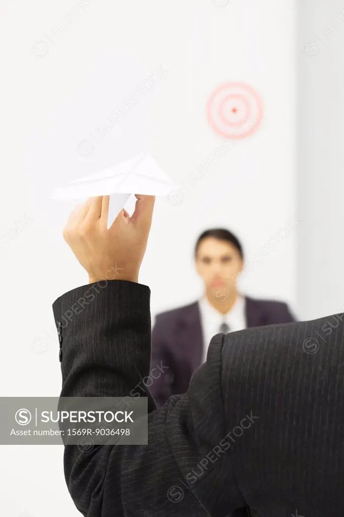 Man holding paper airplane, aiming at target over colleague´s head, cropped view