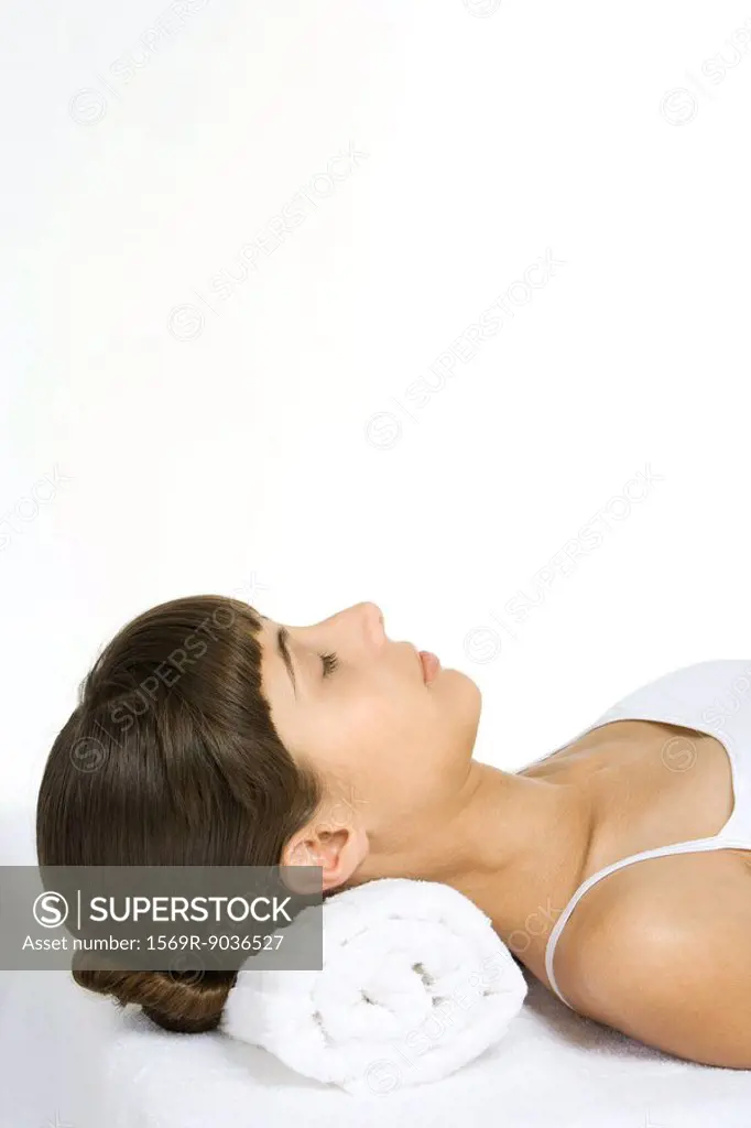 Woman lying on back with eyes closed, using towel as a pillow, cropped view